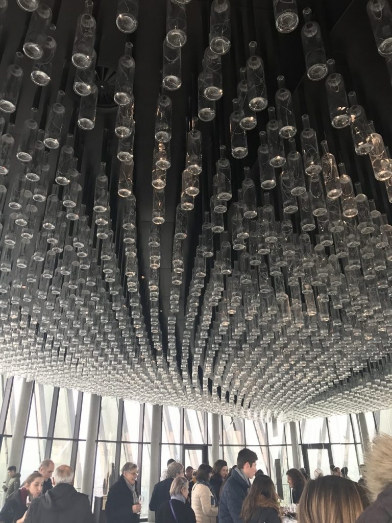 A high, lengthy ceiling is covered with wine bottles, the necks of which are attached to the ceiling.