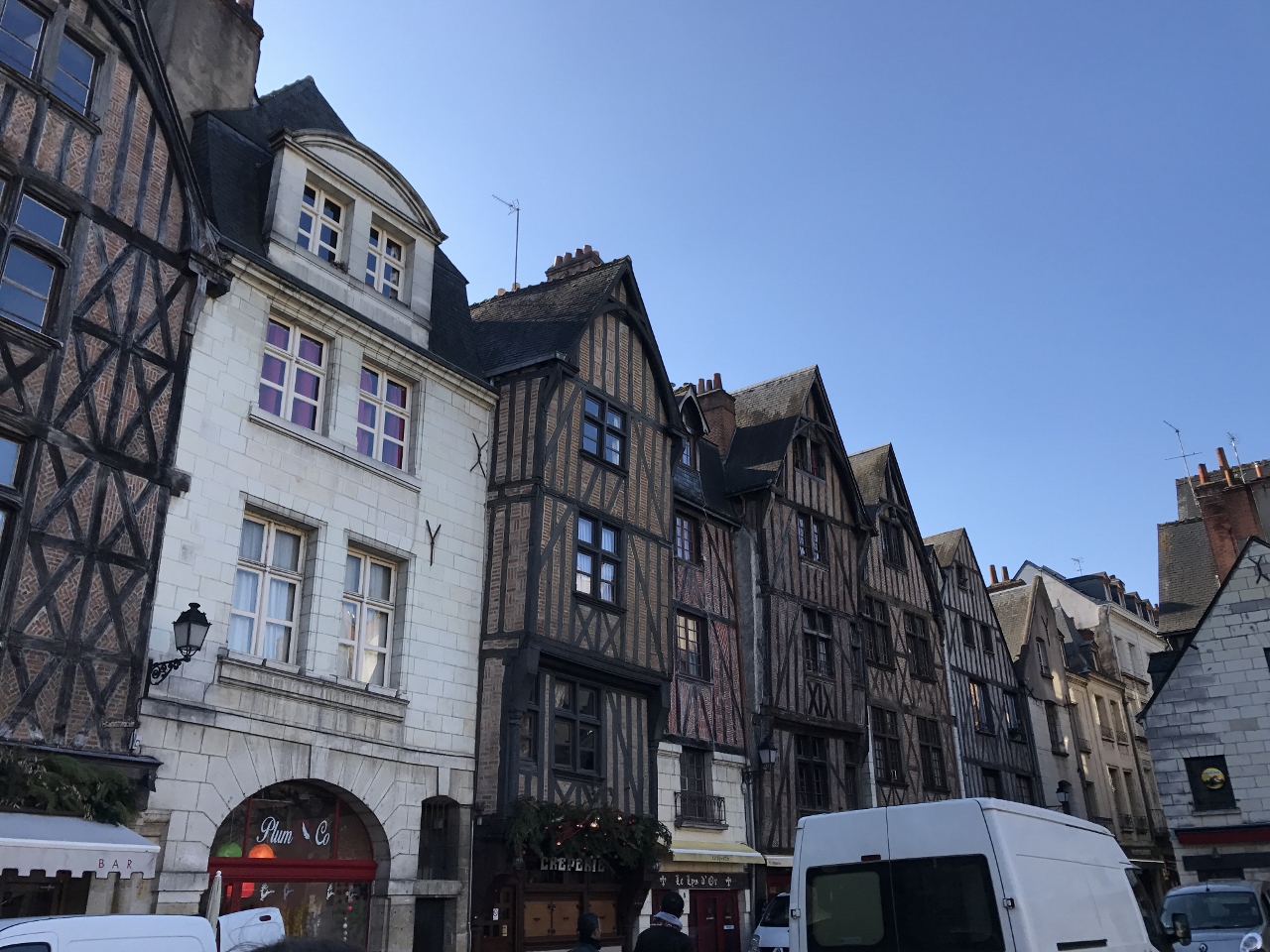 Tall, latticed brown and white buildings line a street with storefronts and cars