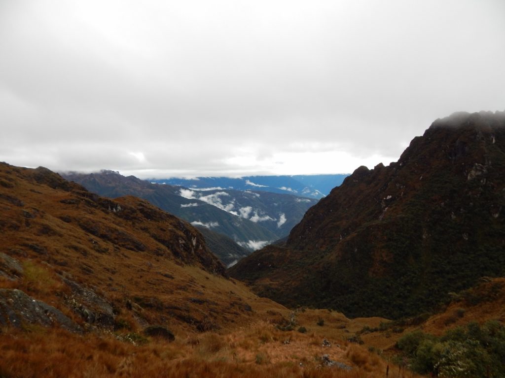 Yellow-green hills, mountain peaks, and snowcapped mountains in the distance underneath a cloudy sky