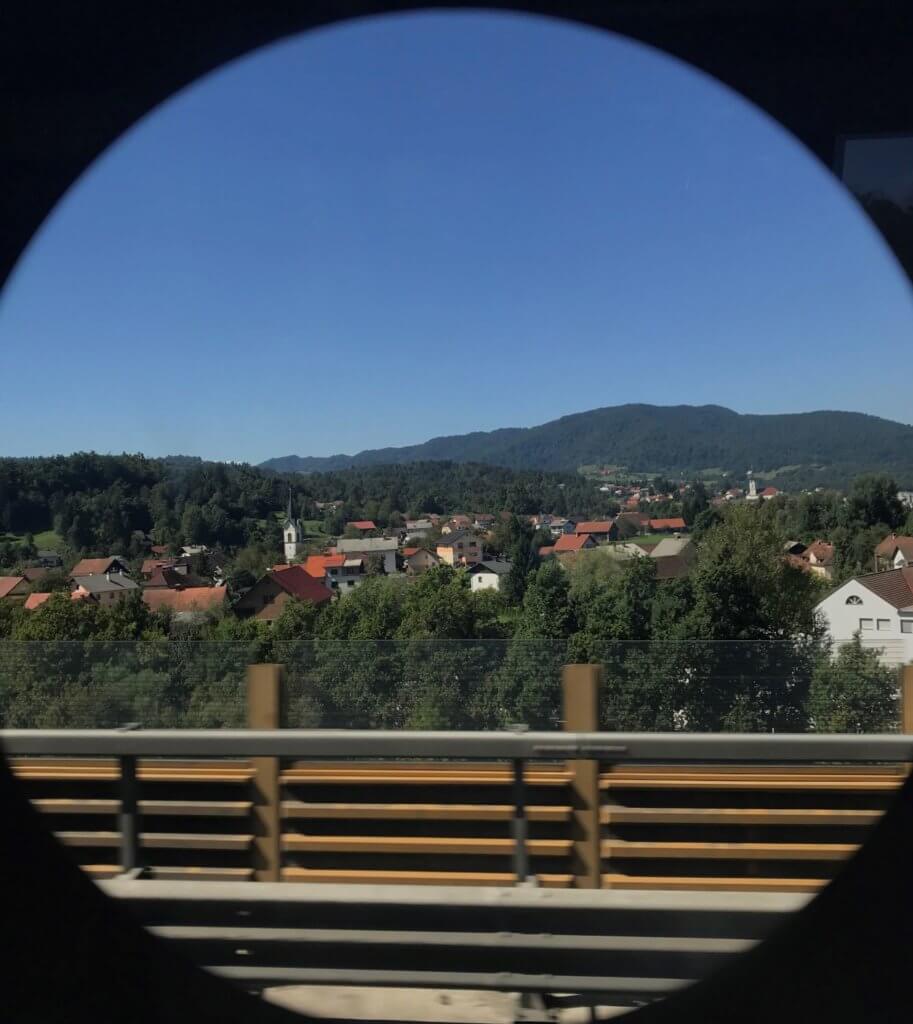 A circular view of stucco rooftops and distant mountains from a bus window