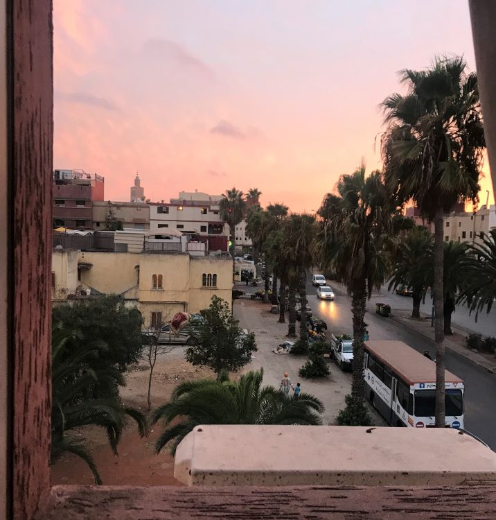 A window view of palm trees, cars, and the setting sun from Mohammedia, Morocco.