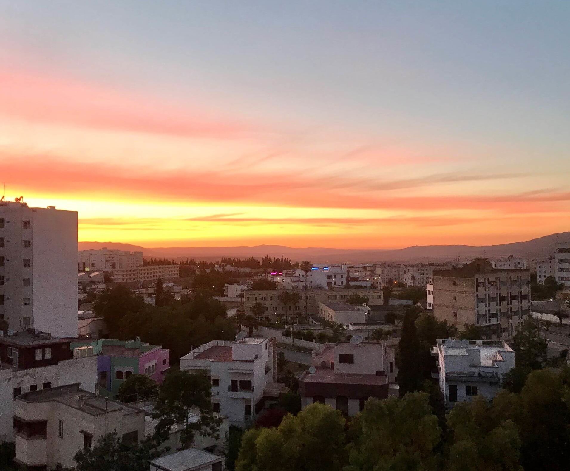 Streaks of orange and pink cover the sky. Buildings below are slowly darkening as the sun sets over them.